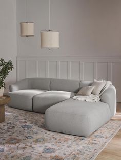 a large gray couch sitting on top of a rug next to a wooden table and lamp