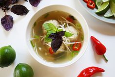 a white bowl filled with soup next to sliced limes and red peppers on a table