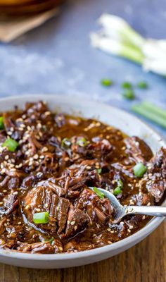 a white bowl filled with beef and rice on top of a wooden table next to green onions