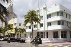 a white building with palm trees on the side of it and people riding bikes in front