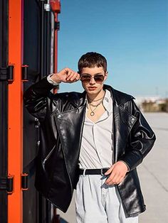 a young man wearing sunglasses and a leather jacket standing in front of an orange structure