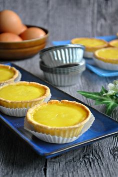 there are three pies on the blue plate next to some flowers and eggs in bowls