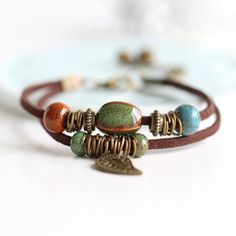 Elevate Your Wrist Game with Artisan Charm Discover the timeless beauty of our Handcrafted Ceramic Bead Leather Bracelets. Each piece is a symphony of carefully selected, earth-toned ceramic beads, harmoniously paired with delicate metal accents to create a melody of rustic elegance. The centerpiece of each bracelet is a beautifully detailed leaf charm, a gentle reminder of nature's serene elegance that dangles gracefully from the sturdy leather band. Crafted for Uniqueness No two beads are the same. Shaped, glazed, and fired to perfection, the ceramic beads offer a touch of unique artistry to your ensemble. Their robust earthy hues are inspired by the natural world, bringing a warm, bohemian vibe to any outfit. Comfort Meets Style Designed with wearability in mind, our bracelets boast an Ceramic Beads Bracelet, Handmade Ceramic Jewelry, Wrap Armband, Leather Charm Bracelets, Cerámica Ideas, Boho Style Jewelry, Bead Chain, Strand Bracelet, Ceramic Jewelry