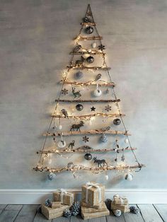 a small christmas tree with lights and presents under it on the floor in front of a wall