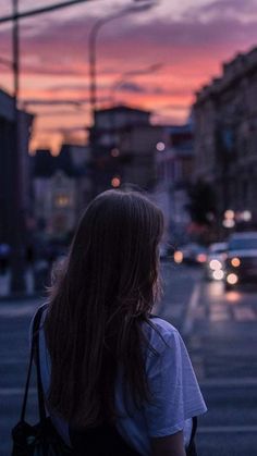 a woman is walking down the street at sunset