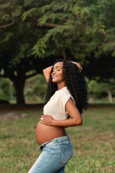 a pregnant woman standing in the grass with her hands on her head and looking up