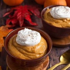 two small bowls filled with pumpkin pudding on top of a wooden table next to oranges