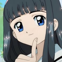 a girl with long black hair and blue eyes is holding her hand up to her face