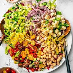 a large salad on a white plate topped with red onions, tomatoes and chickpeas