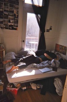 two people laying on top of a bed in a bedroom next to a large window