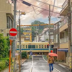 a woman with an umbrella walks down the street in front of a train on a cloudy day