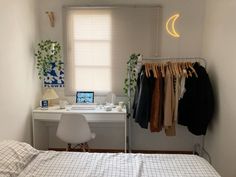 a bedroom with a bed, desk and clothes hanging on the rack in front of a window