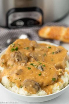 a white bowl filled with mashed potatoes covered in gravy next to an instant pressure cooker