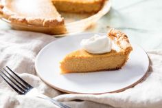 a slice of pumpkin pie on a white plate with a fork next to the pie