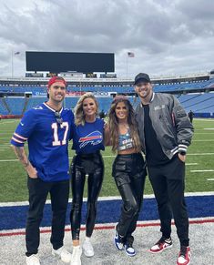 three people posing for a photo in front of an empty football field with the bills on it