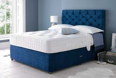 a bed with blue upholstered headboard and foot board next to a window