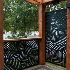 an outdoor privacy screen with black leaves on the outside and wood frame around it, in front of a tree