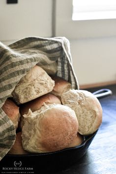 a basket filled with rolls sitting on top of a wooden table next to a window