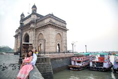 a man and woman standing on the edge of a bridge next to boats in the water