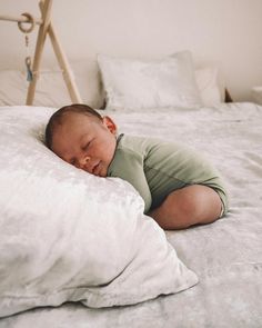 a baby sleeping on top of a white bed next to a wooden frame and pillows