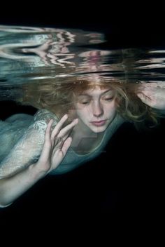 a woman is submerged in the water with her hands on her head and looking down