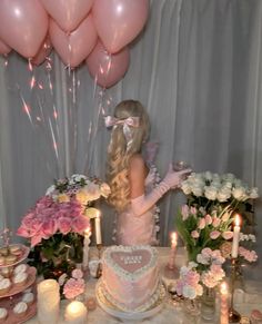 a woman standing in front of a cake with pink flowers on it and balloons behind her