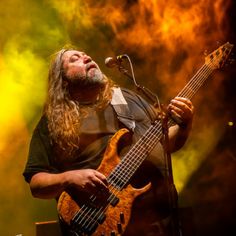 a man with long hair and beard playing a guitar in front of a microphone on stage