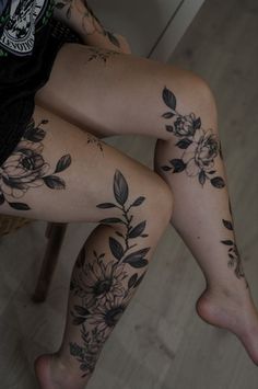 a woman's legs with flowers and leaves tattooed on her leg, sitting in a chair