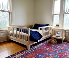 a bedroom with two windows and a rug on the floor in front of it,