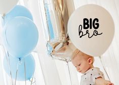 a baby is sitting in front of balloons with the word big bro written on them