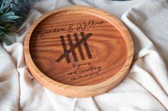 a personalized wooden plate with the names and date engraved on it sitting on a white cloth