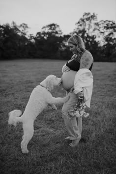 a pregnant woman playing with her dog in a field at sunset or sunrise hour, black and white photograph