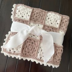 a crocheted blanket with a white bow on it sitting on a wooden floor