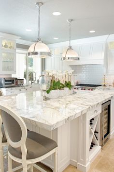 a large kitchen with marble counter tops and white cabinets, along with two bar stools