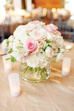 a vase filled with white and pink flowers sitting on top of a table next to candles