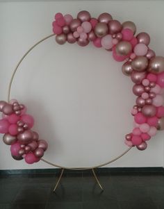 a circle made out of pink and silver balloons on a metal stand in front of a white wall