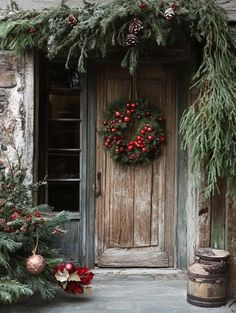 a wreath is hanging on the front door of an old stone building with evergreen and red berries