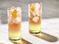 two glasses filled with lemonade and ice on top of a marble table next to each other