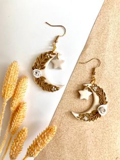 two pairs of earrings sitting next to each other on a white surface with dried flowers