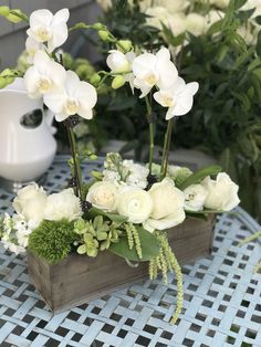 white flowers and greenery sit in a wooden box on a blue tableclothed surface