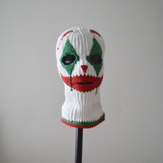 a white and green knitted face mask on a black stick with red, white, and green stripes