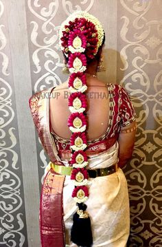 a woman wearing a red and white saree with flowers in her hair, standing against a wall