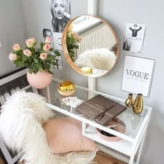 a white desk with a mirror, vase and flowers on it next to a chair