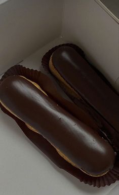 two chocolate covered donuts sitting in a box on top of a counter next to each other