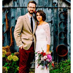 a bride and groom standing in front of an old wooden shed with flowers on it