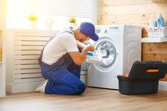 a man in blue overalls and white shirt working on a washing machine