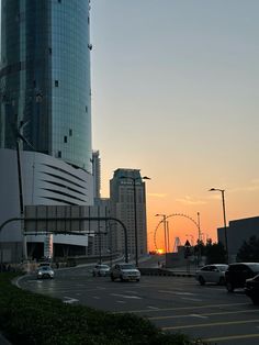 the sun is setting in front of a tall building and cars are driving down the street