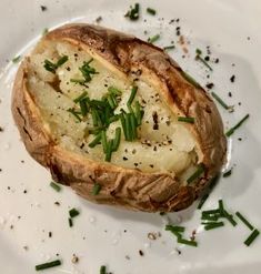 a baked potato on a white plate topped with green onions