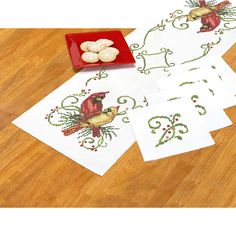 four cross - stitch cards with birds on them next to a bowl of small cookies