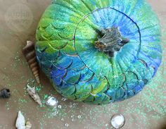 a blue and green painted pumpkin sitting on top of a table next to seashells